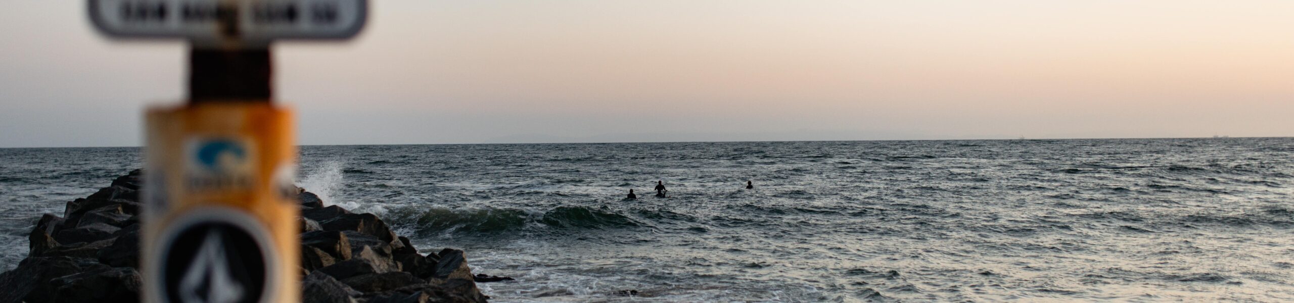 Pacific ocean from the shore with an out of focus sign and rocks in the foreground